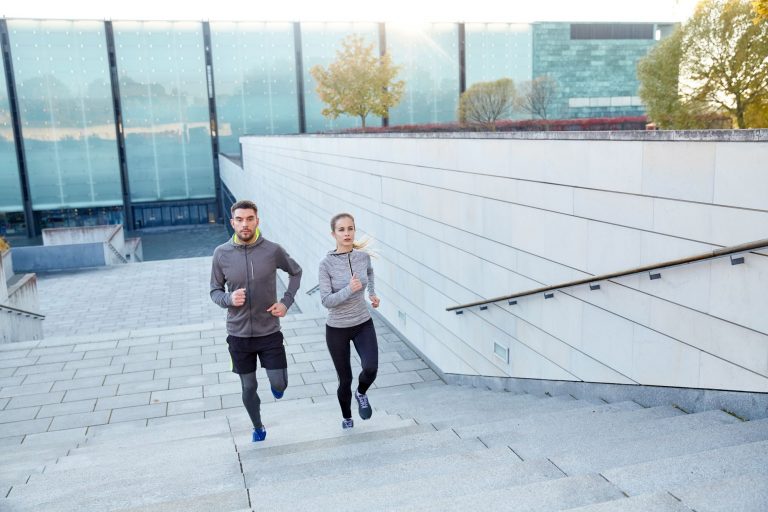 Um casal se exercitando, subindo escadas e seguindo dicas do seu médico para começar a fazer exercícios físicos.