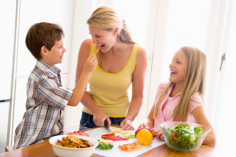Mãe e dois filhos felizes ao redor da mesa, a mãe segue dicas para cuidar da saúde da família.