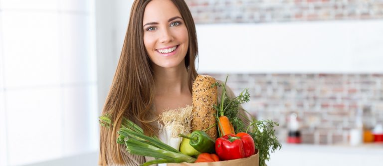 Mulher com cesta de alimentos e feliz por consegui-los digerir adequadamente devido ao uso dos probióticos.