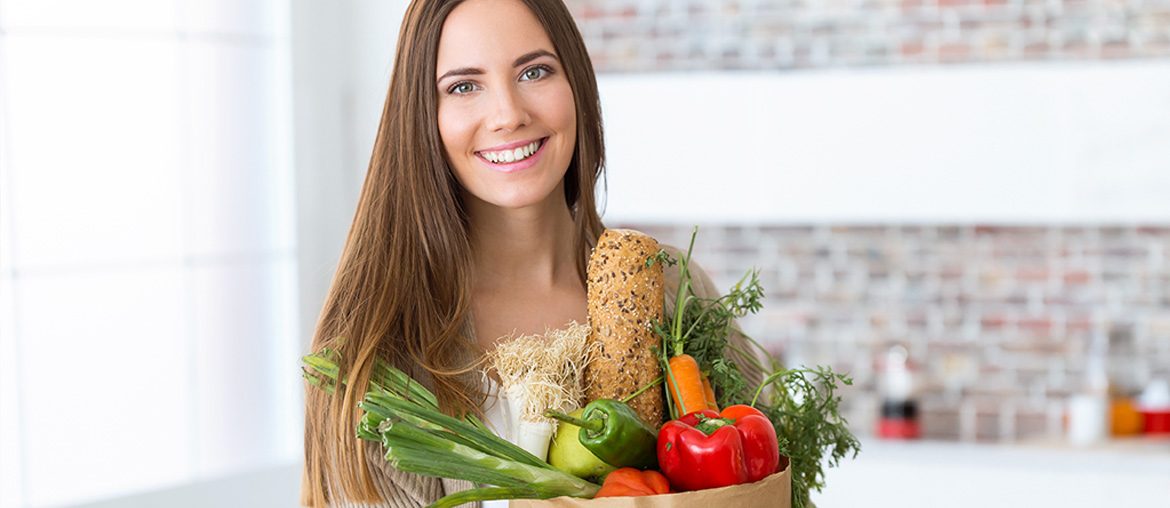 Mulher com cesta de alimentos e feliz por consegui-los digerir adequadamente devido ao uso dos probióticos.
