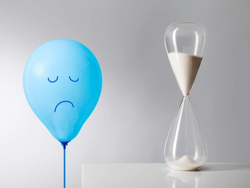 Balão azul com desenho triste e ampulheta ao lado.