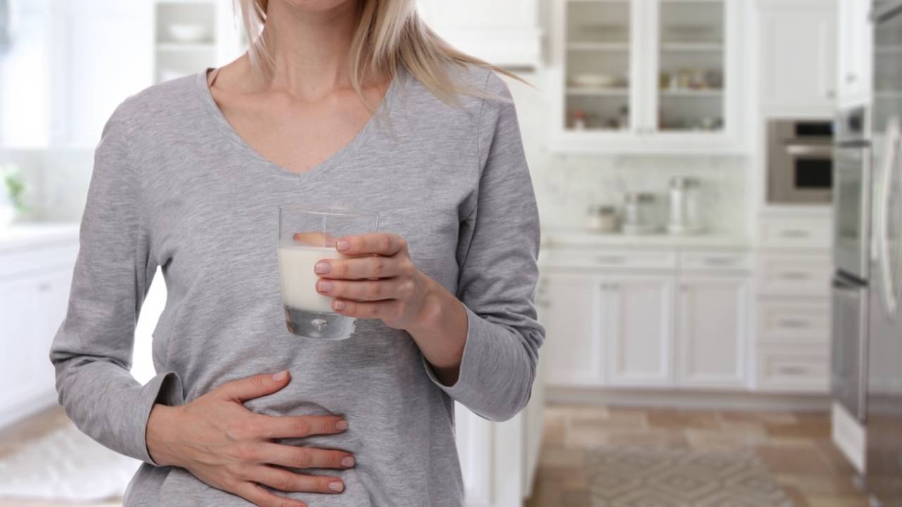 Mulher segurando um copo de leite e com a outra mão na barriga.