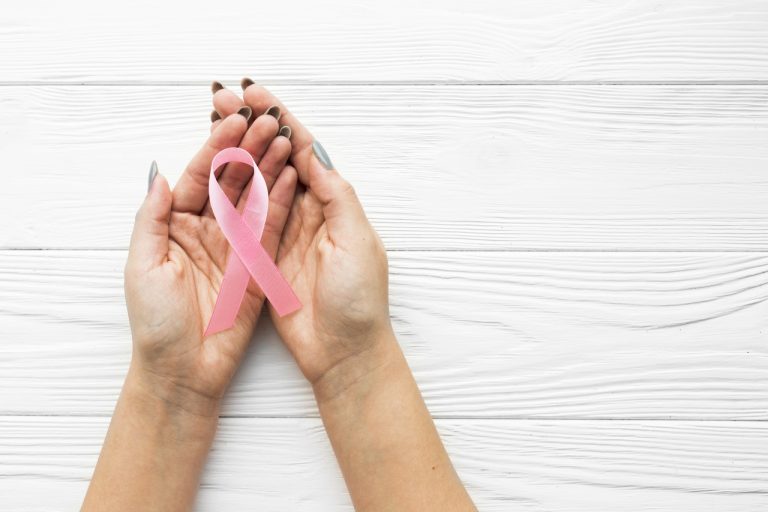 Mulher com laço ícone do Outubro rosa na mão, simbolizando combate ao Câncer de Mama