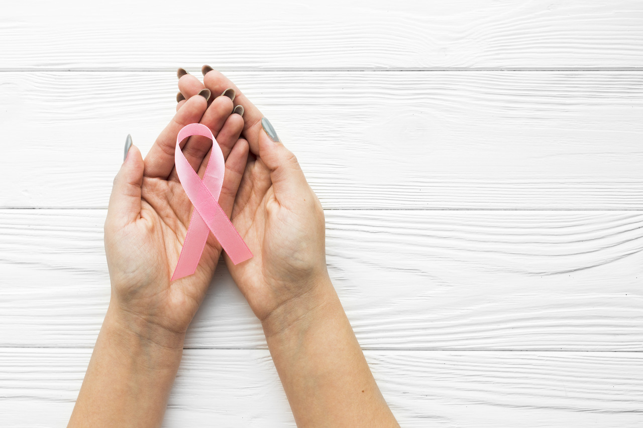 Mulher com laço ícone do Outubro rosa na mão, simbolizando combate ao Câncer de Mama