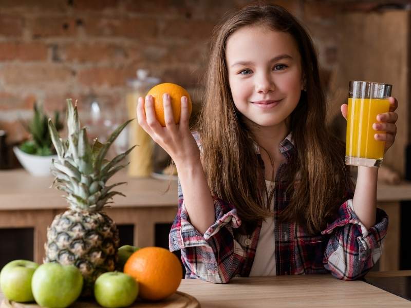 Menina com alimentos saudáveis em sua frente.