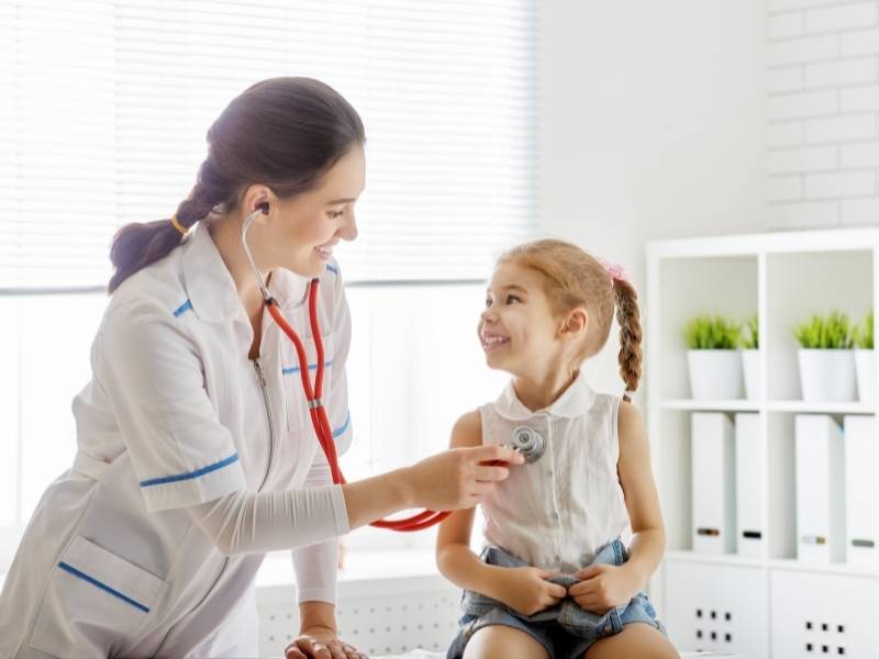 Médica pediatra auscultando coração de criança.