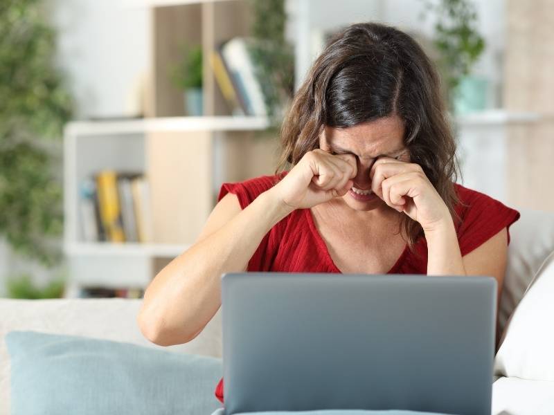 Mulher sentada em frente ao computador com os olhos coçando.