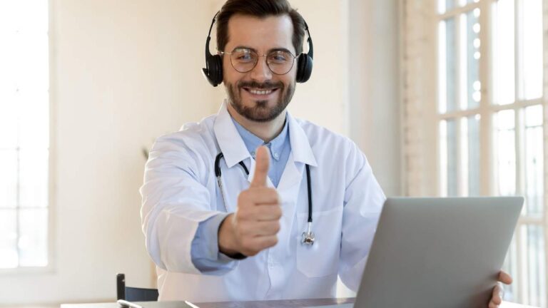 Médico em frente ao computador fazendo sinal de joia.