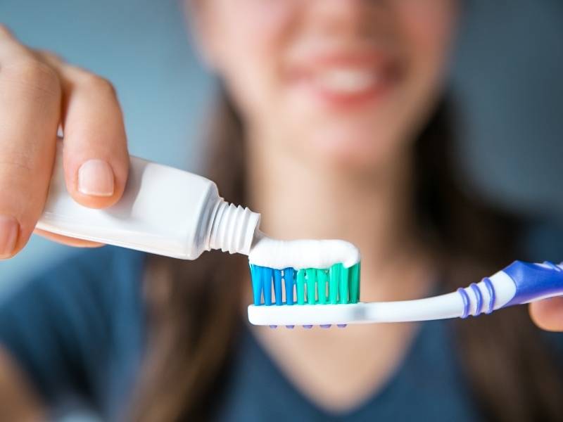 Mulher colocando creme dental na escova para fazer higienização bucal.