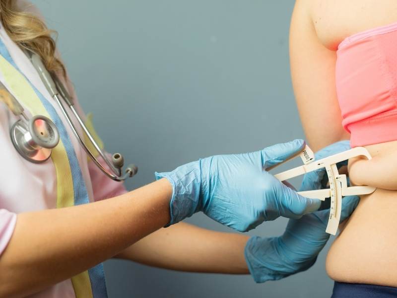 Médica realizando medição de gordura corporal em paciente mulher.