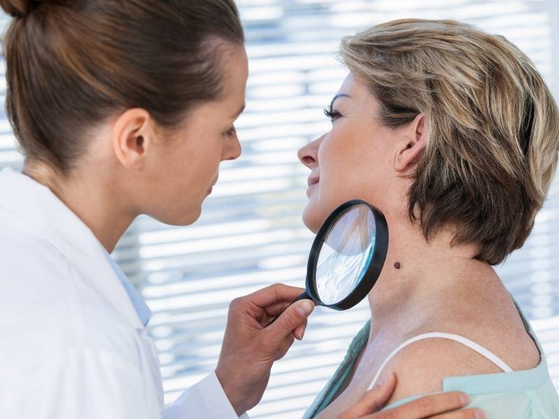 Médica dermatologista examinando pinta no pescoço de paciente.