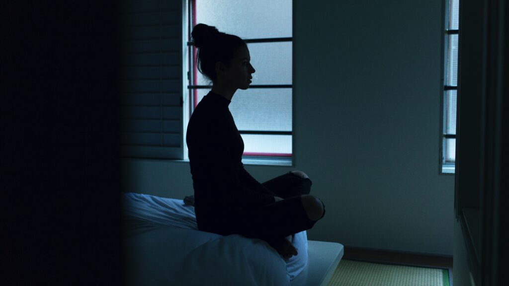 Mulher sentada na cama com dificuldades para dormir.