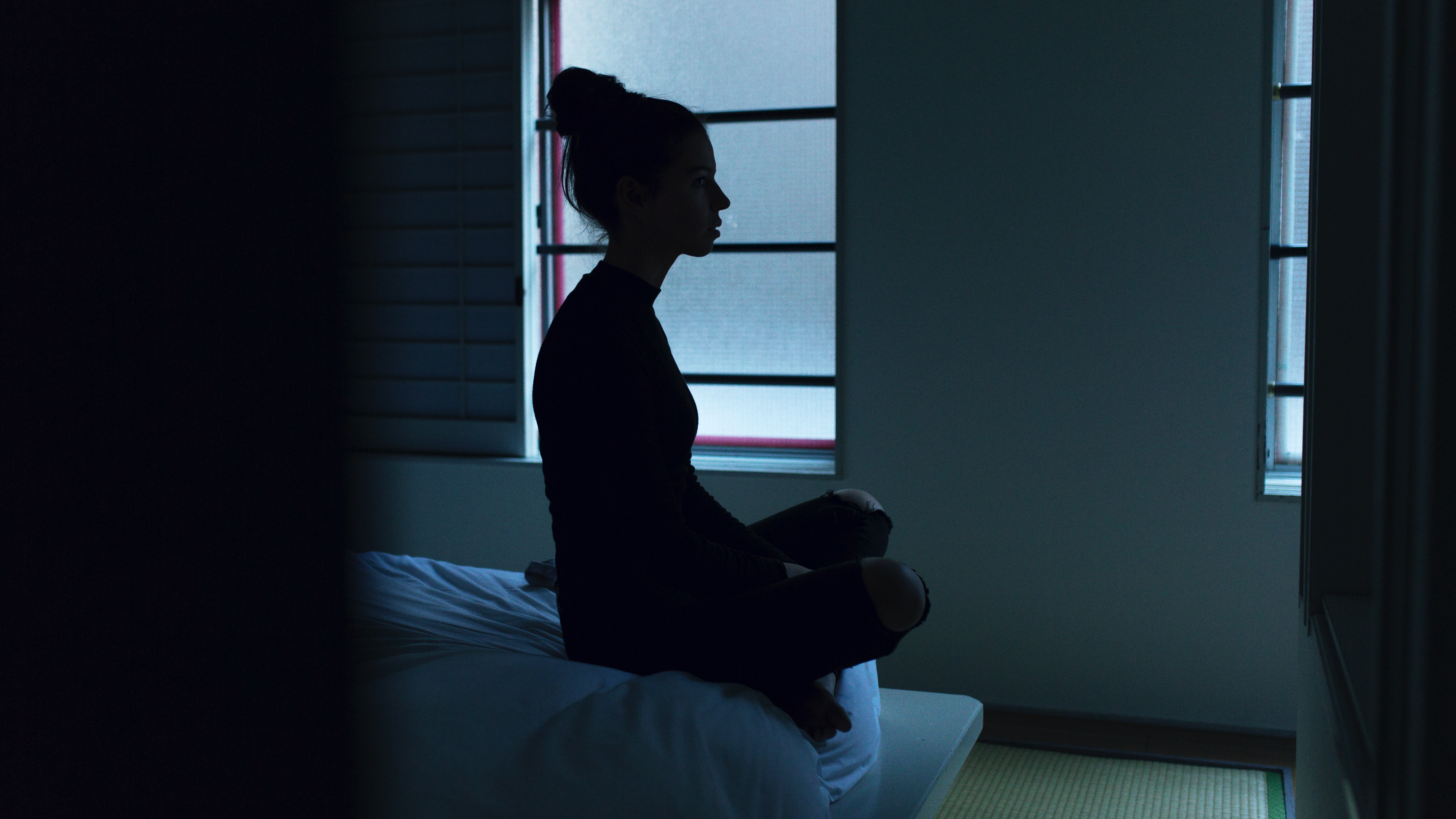 Mulher sentada na cama com dificuldades para dormir.