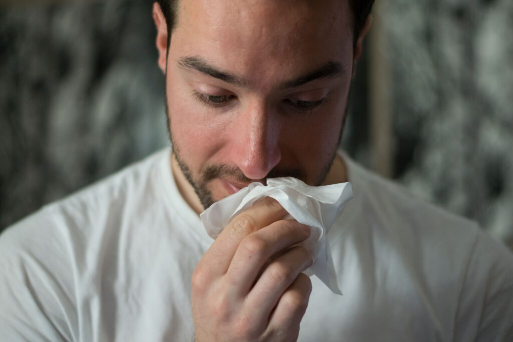 Homem gripado com lenço de papel na mão.