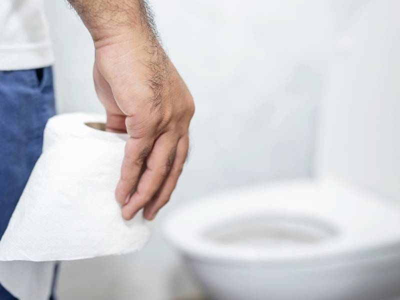 Homem no banheiro segurando um rolo de papel higiênico.