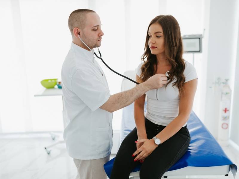 Médico com estetoscópio auscultando batimentos cardíacos de mulher.