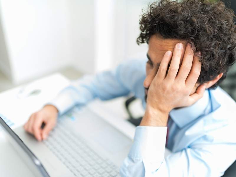 Homem com a mão no rosto em frente ao computador desanimado.