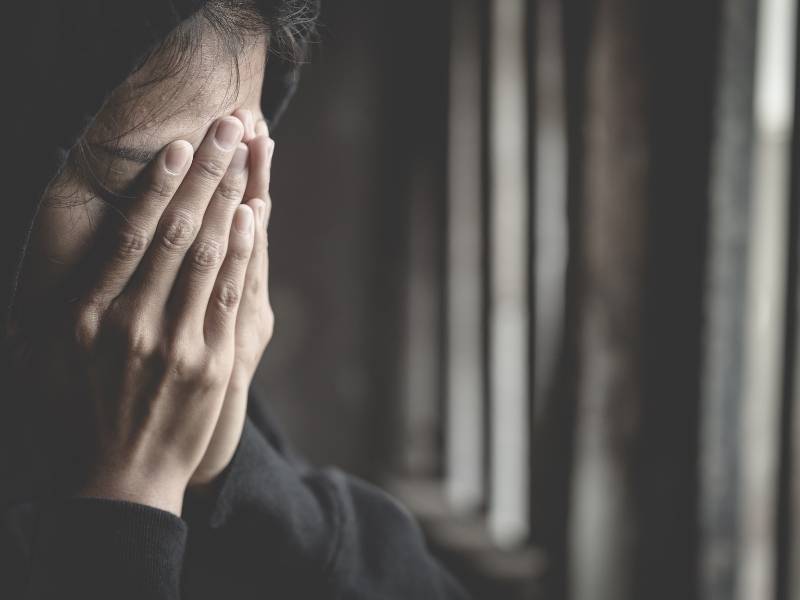 Mulher jovem com as mãos no rosto com a feição triste.