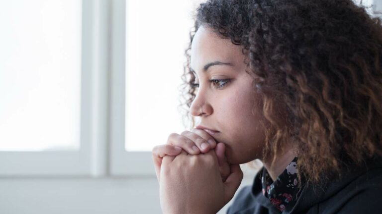 Mulher jovem com depressão sentada com a mão no queixo.