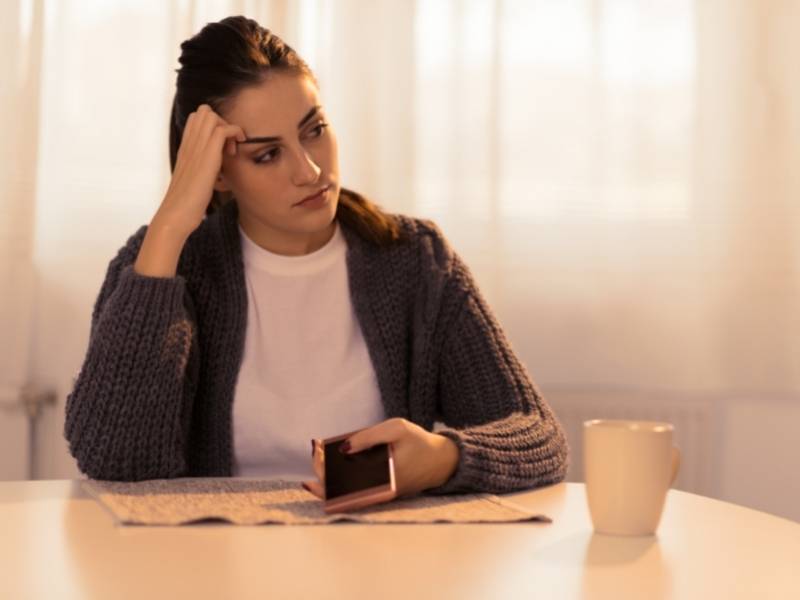 Mulher jovem sentada sozinha com celular na mão.
