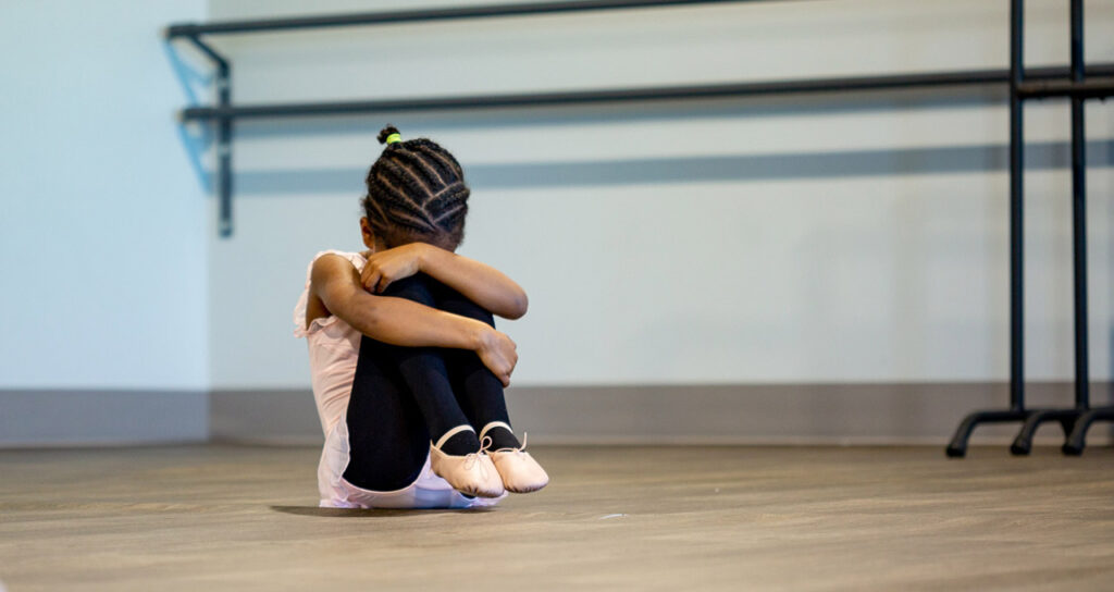 menina negra sentada chorando na aula de ballet