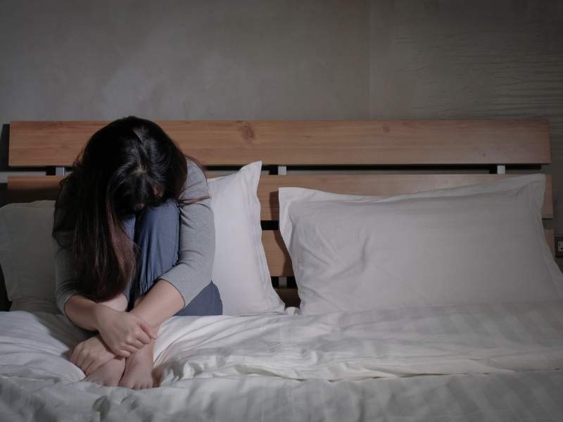 Mulher sentada na cama com possível quadro de depressão.