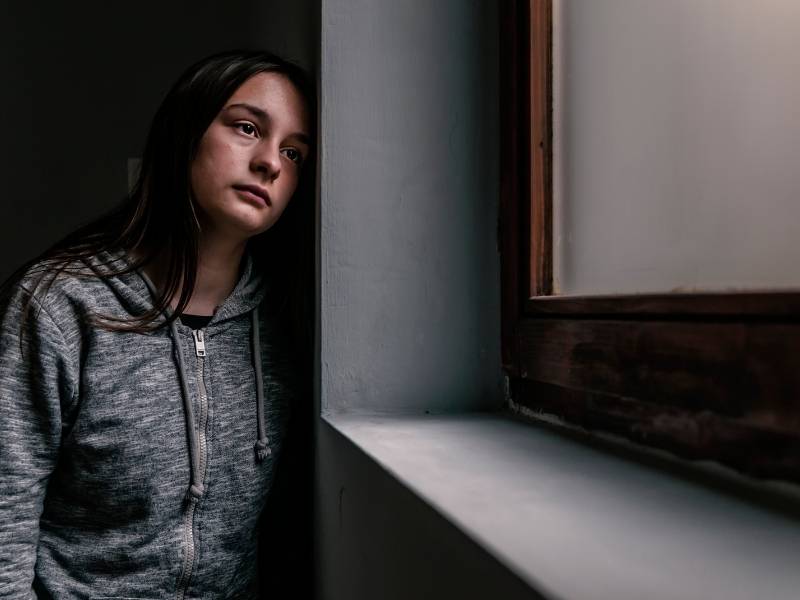 Mulher jovem triste olhando pela janela.