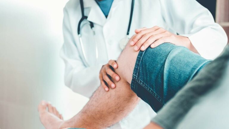 Médico ortopedista examinando joelho de paciente.