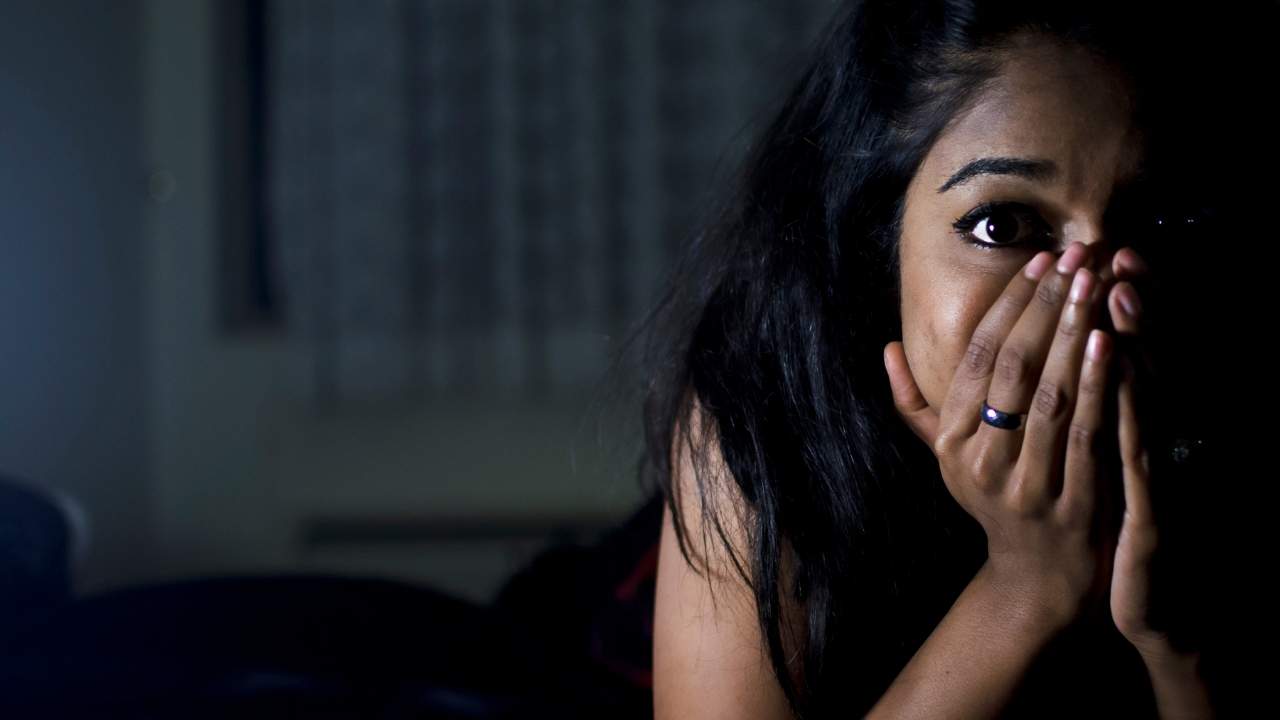 Mulher jovem com a mão na boca durante crise de pânico.