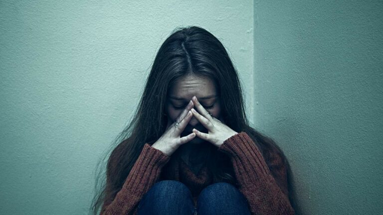 Mulher jovem triste sentada no chão chorando.