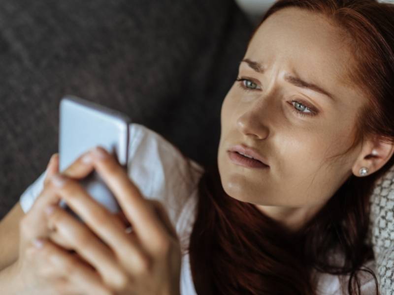 Mulher jovem deitada usando celular.