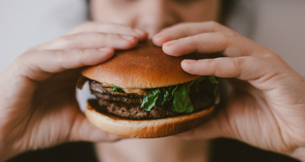 pessoa comendo hambúrguer vigorosamente, o que pode ser sinal de ansiedade