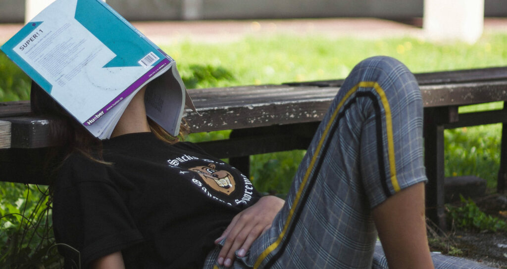 menina estudante com livro no rosto sinalizando exaustão, sintoma da ansiedade