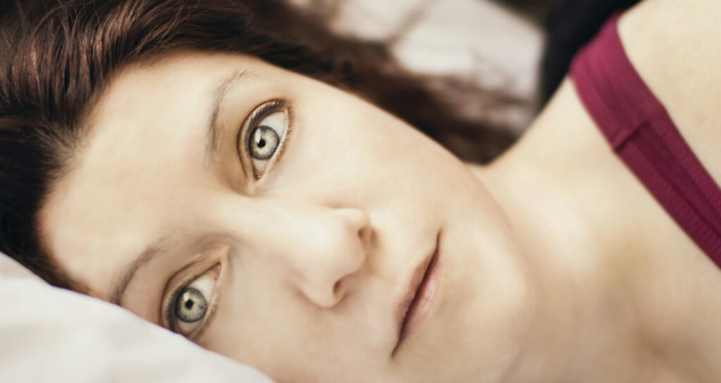 mulher deitada na cama com os olhos abertos, demonstrando sua insônia