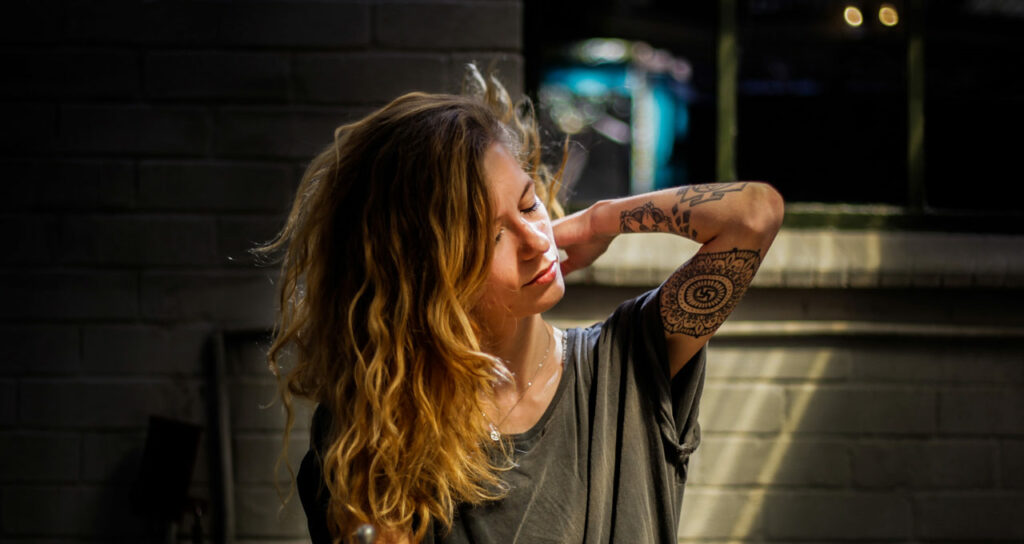 mulher com tatuagens colocando a mão nas costas para aliviar sua tensão muscular pela ansiedade