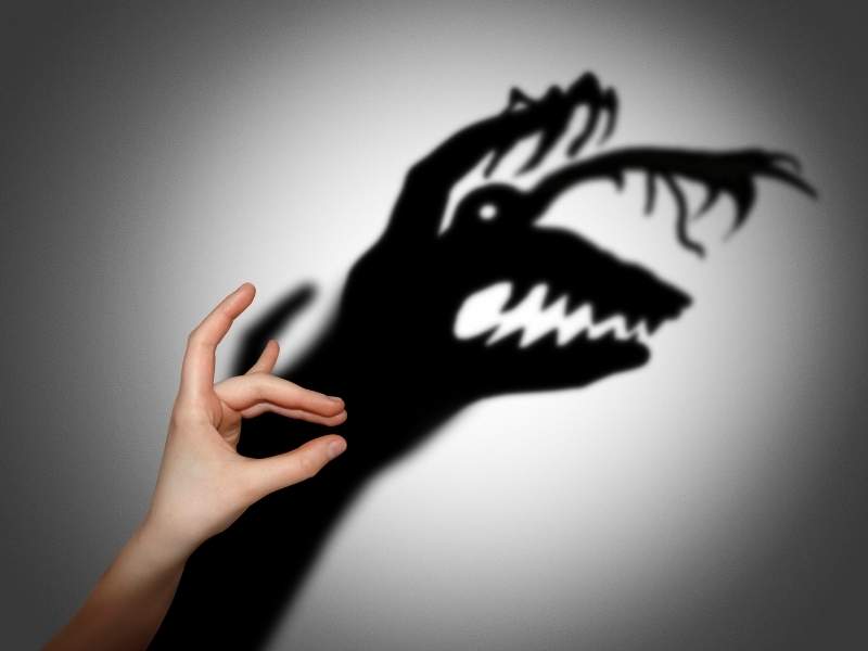 Ilustração de mão com sombra de monstro simbolizando falso medo.