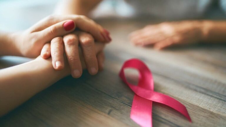 Duas pessoas com as mãos dados com o símbolo da prevenção do câncer de mama ao lado.
