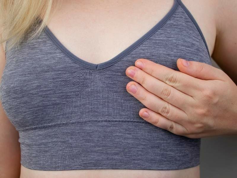 Mulher jovem com a mão no seio com possível nódulo.