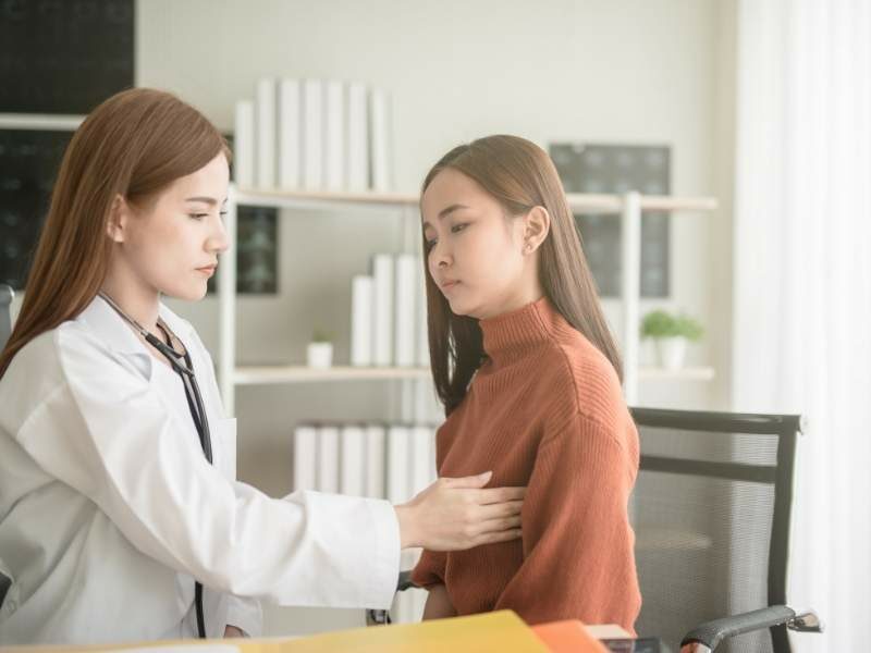 Médica mastologista realizando exame clínico de palpação em mulher jovem.