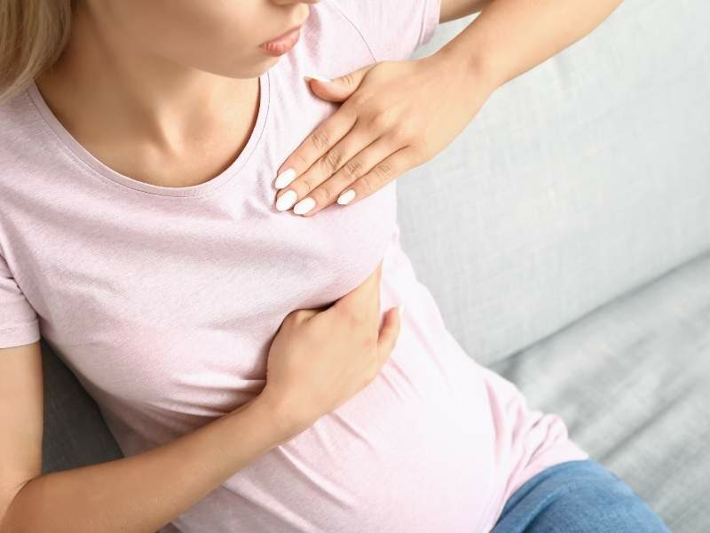 Mulher jovem com a mão no seio com possível quadro de mastite.