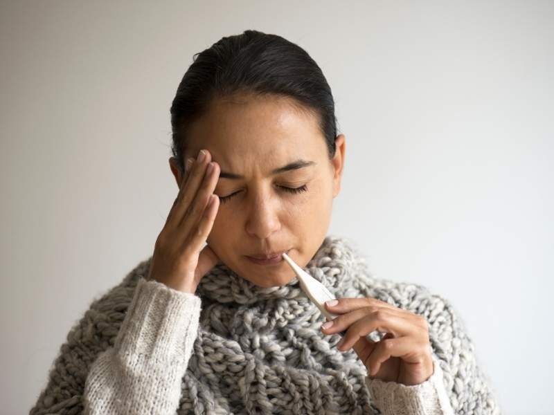Mulher com dengue e febre medindo temperatura.