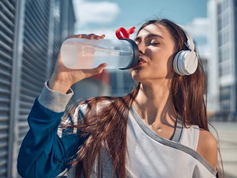 Mulher jovem bebendo agua após atividade física.