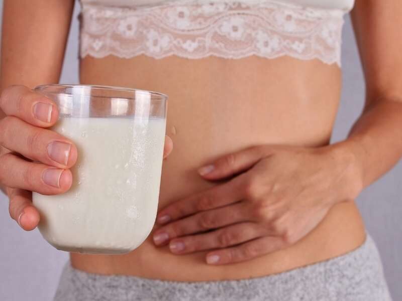 Pessoa segurando copo de leite com a mão na barriga.