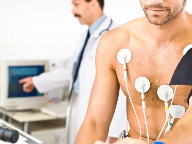 Homem sentado com eletrodos no peito para realizar eletrocardiograma.