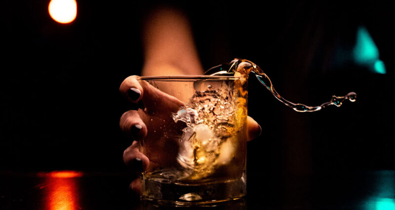 um copo de whiskey sendo colocado na mesa de forma agitada