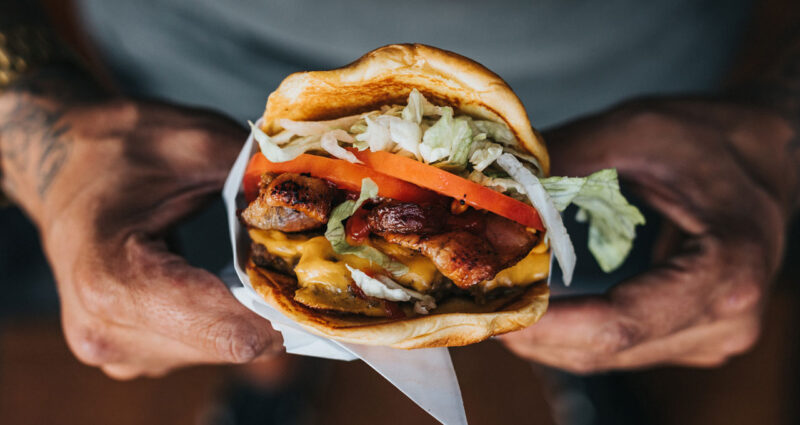 homem segurando um hamburguer gorduroso, o que pode ser uma das causas da insônia
