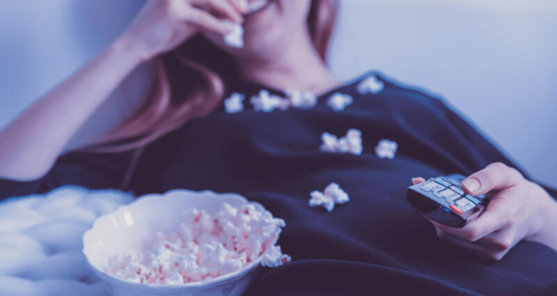mulher comendo pipoca na cama com um estilo de vida sedentário pode ser uma das causas da insônia