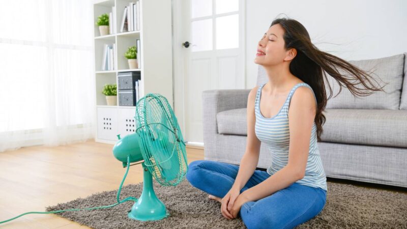 Mulher sentada na frente do ventilador.